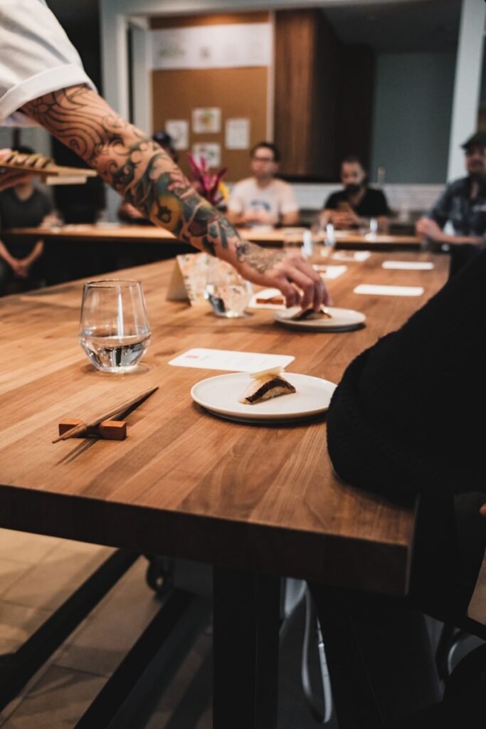 a group of people sitting around a wooden table eating nigiri